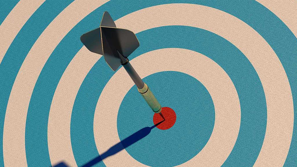 An arrow hits the bullseye of a target with blue and white concentric circles. The image is viewed from above, showing the arrow perfectly centered in the red bullseye. Shadows indicate a light source from the upper right.